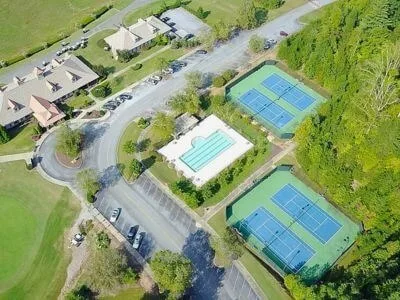 Aerial view of a clubhouse complex with a swimming pool, two tennis court areas, parking and a golf green
